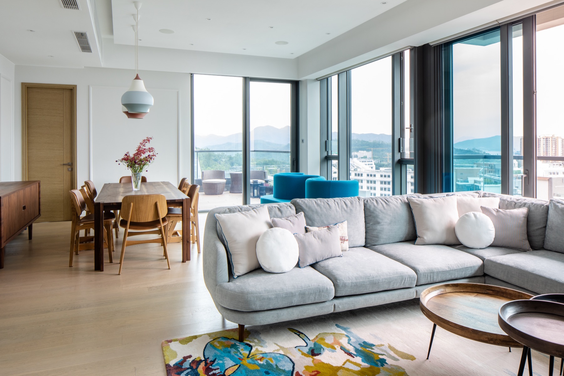 Living and dining room with blue armchairs, a patterned rug and panoramic windows