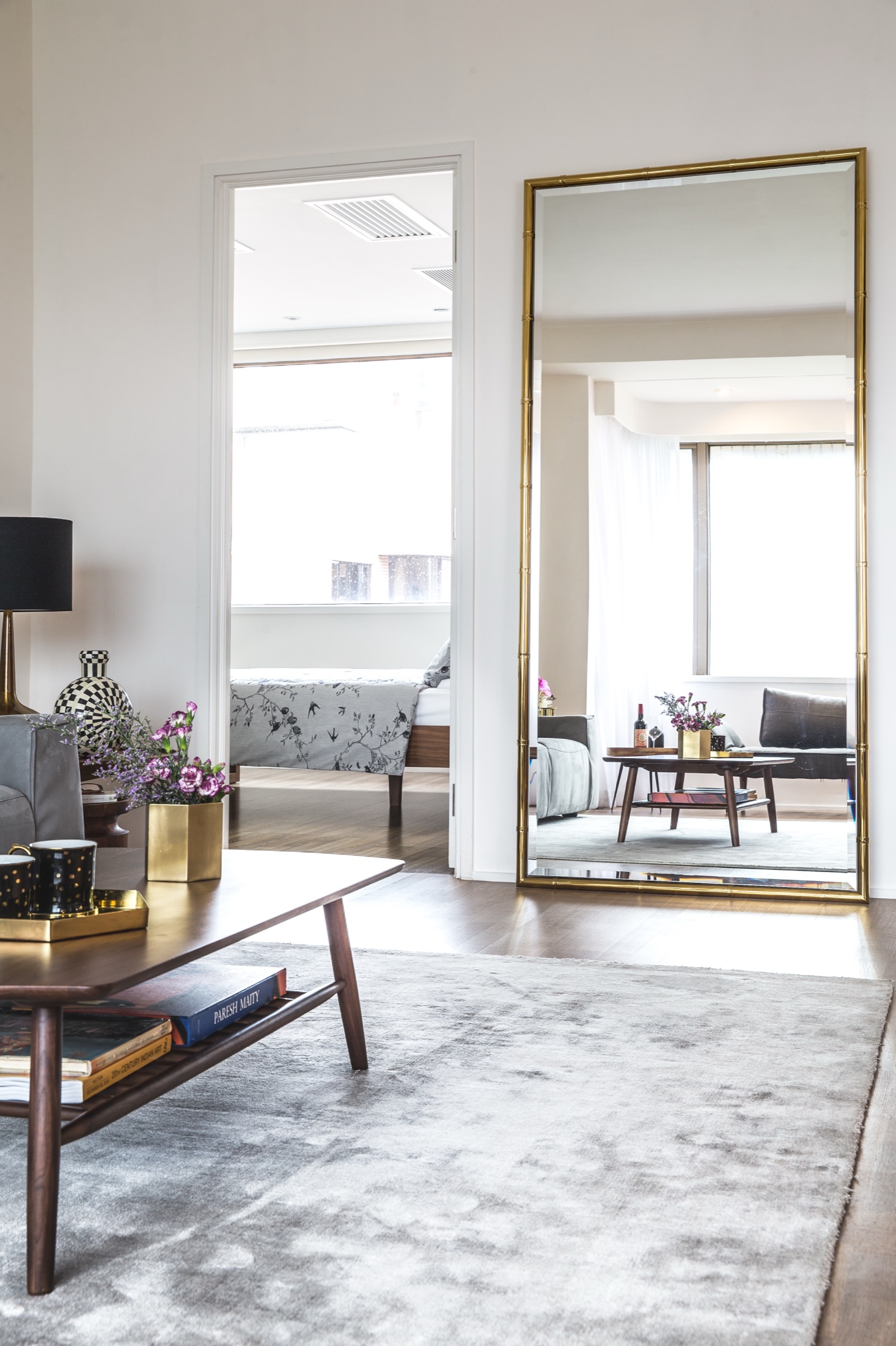 Gold framed mirror reflecting a light living room with timber tables