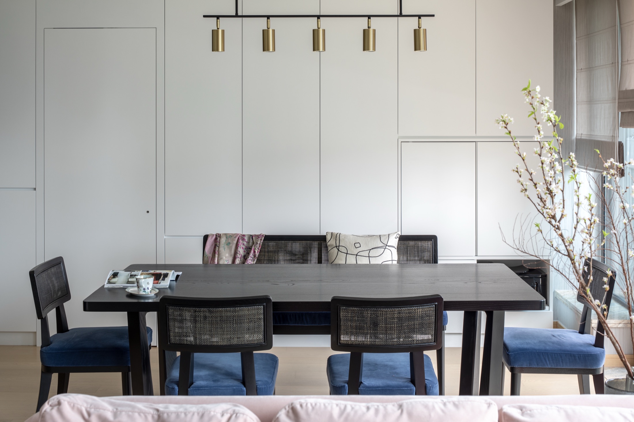 Black dining chairs and a timber table beneath slender gold pendant lights in Softly Sculpted