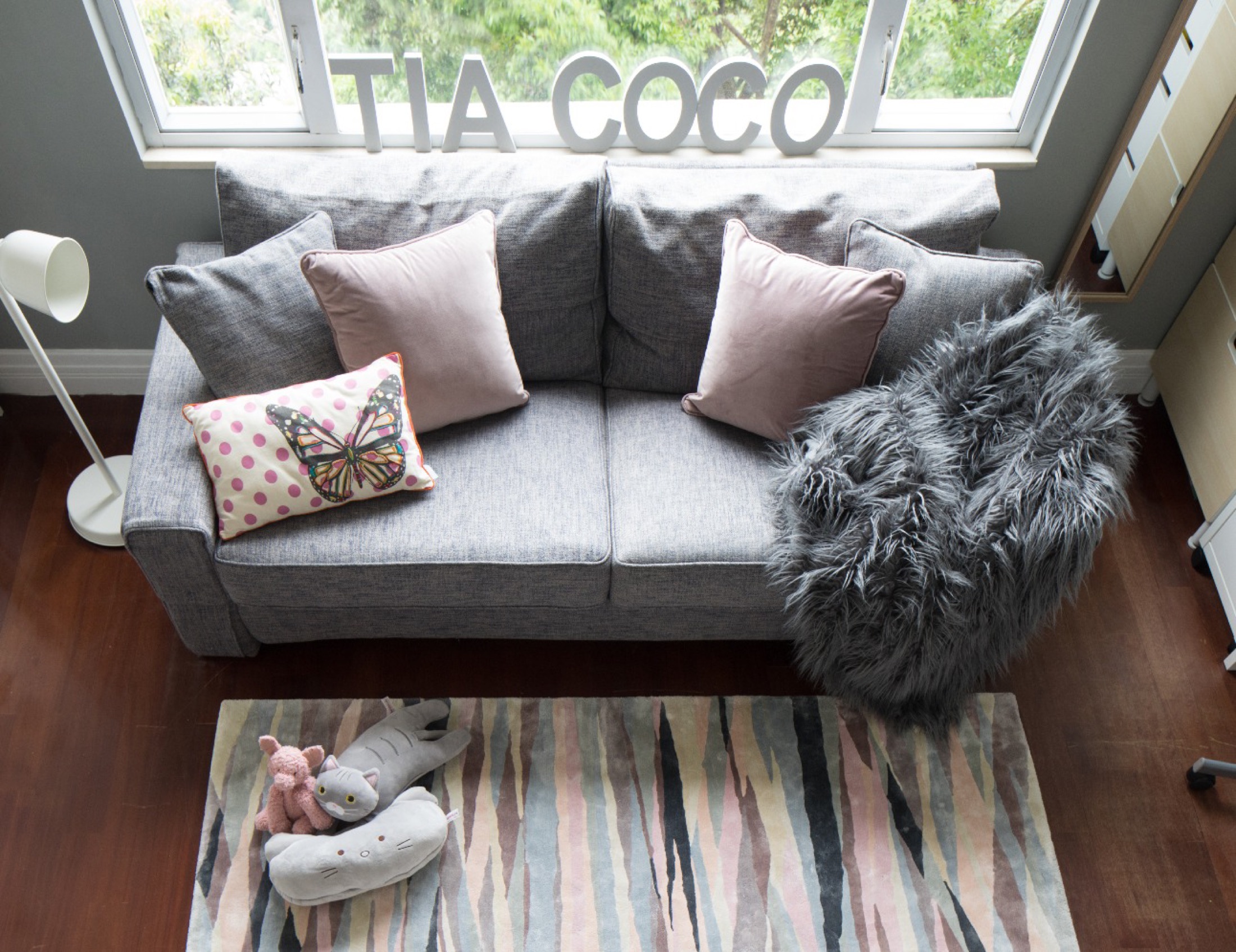 Grey sofa with pink cushions beneath TIA COCO letters in a teen room